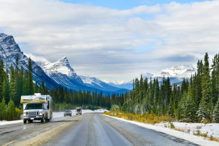 Een camper en auto's rijden over een weg tussen besneeuwde bergtoppen en dennenbossen in Alberta, Canada