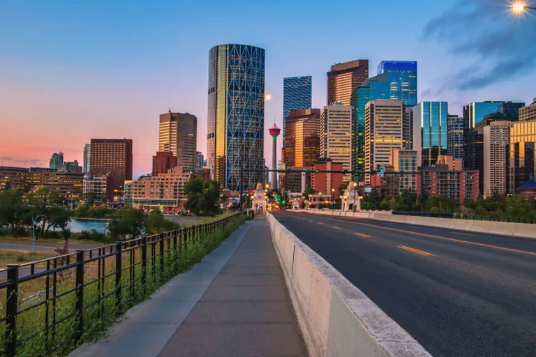 Uitzicht over een brug naar de skyline van Calgary in Alberta, met wolkenkrabbers en de calgary tower tegen een roze avondlucht
