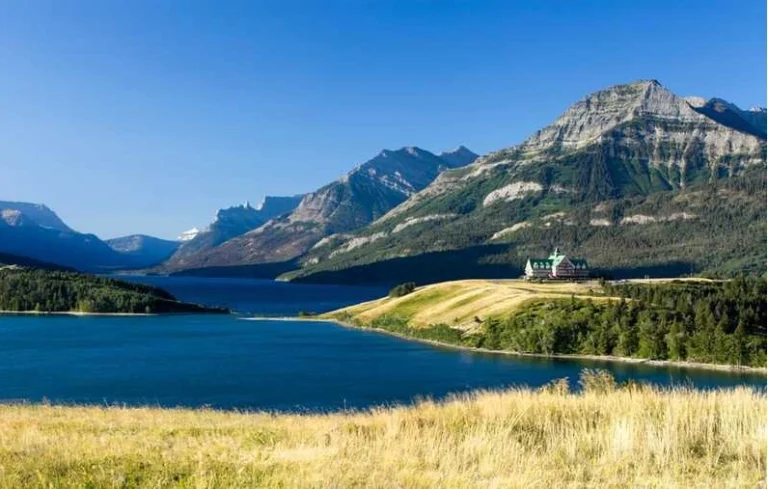 Uitzicht over het blauwe Waterton Lake in Alberta met bergen op de achtergrond en het karakteristieke Prince of Wales Hotel op een landtong