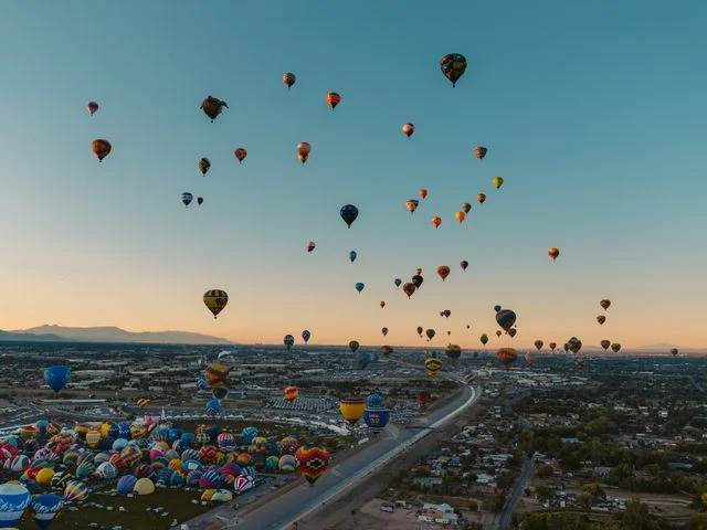 Luchtfoto van tientallen kleurrijke heteluchtballonnen die opstijgen boven de stad Albuquerque bij zonsopkomst met bergen op de achtergrond