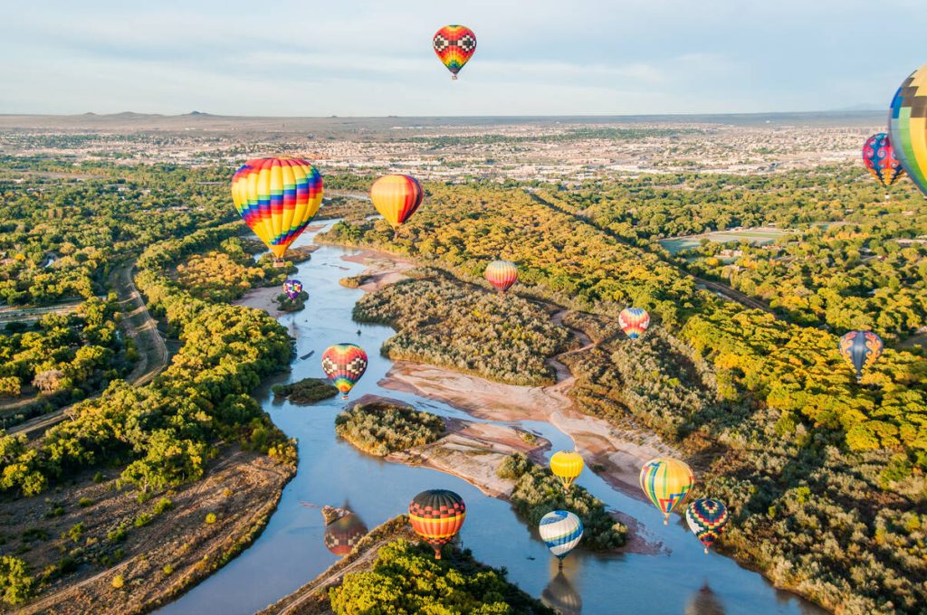 Luchtfoto van tientallen kleurrijke heteluchtballonnen die zweven boven een kronkelende rivier omgeven door bomen bij Albuquerque