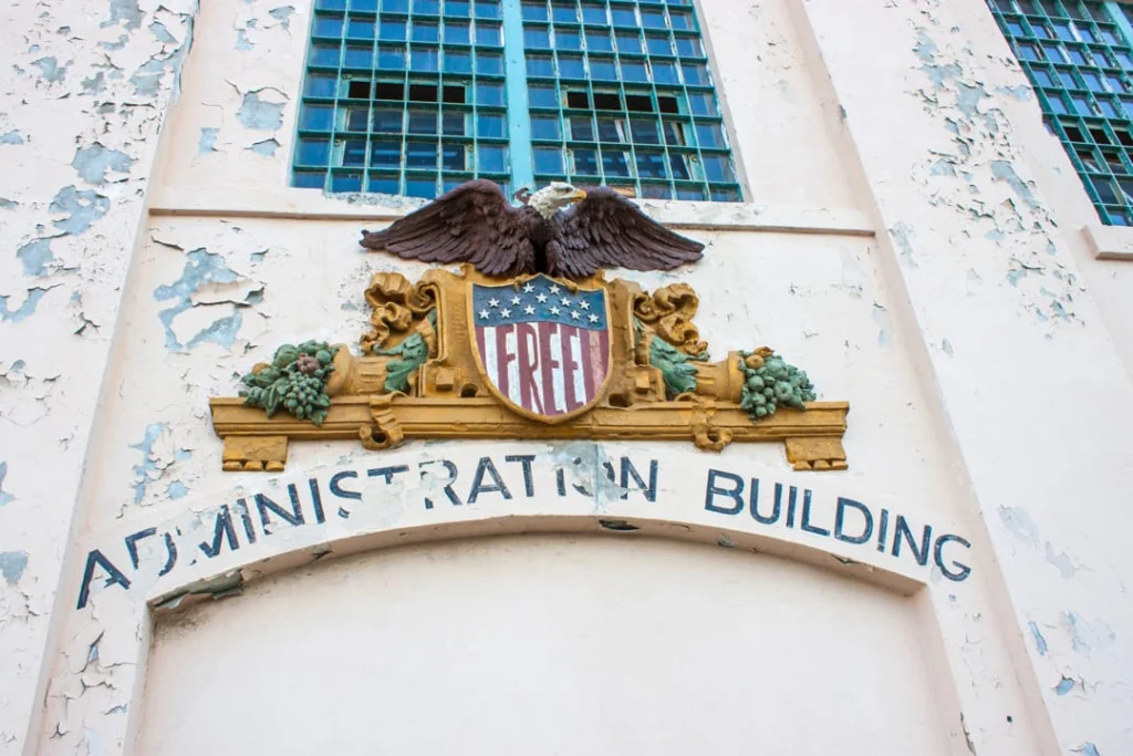 Verweerde gevel van het Administration Building op Alcatraz met een gebeeldhouwde adelaar en Amerikaans wapenschild boven de ingang