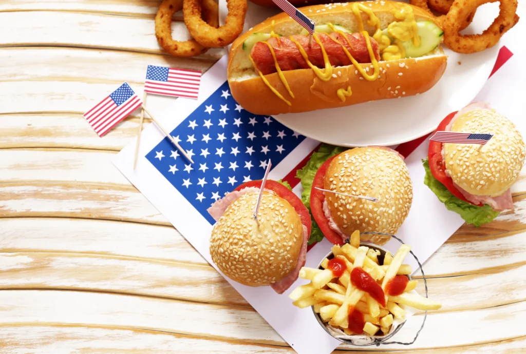 Op een tafel liggen een hotdog, hamburgers, uienringen en een bakje friet met ketchup, versierd met Amerikaanse vlaggetjes