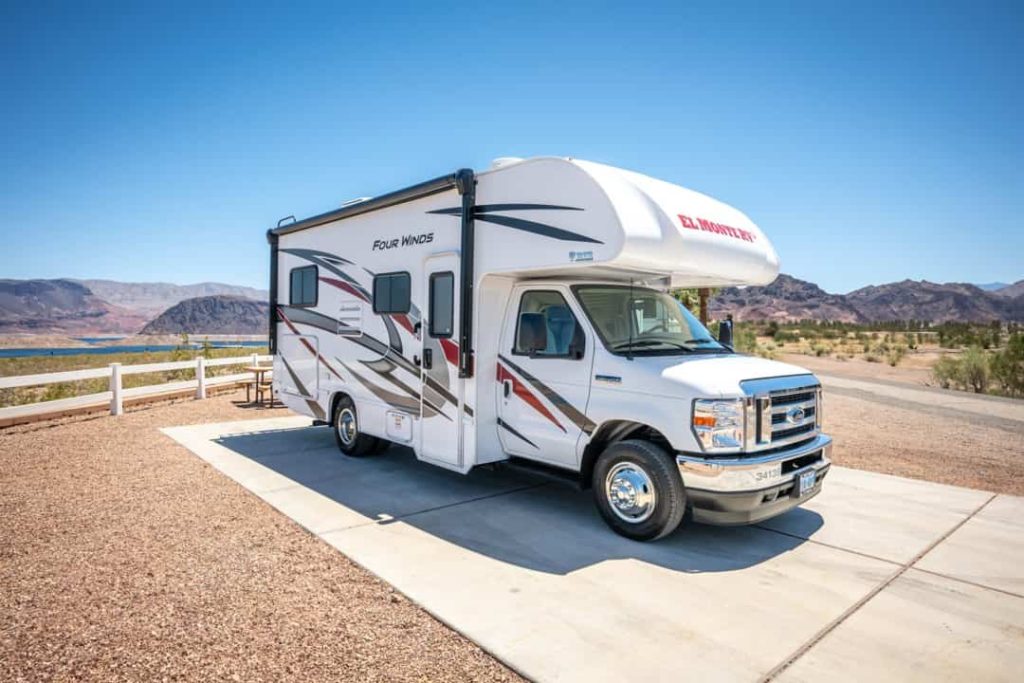 Een compacte witte camper staat geparkeerd op een camperplaats met uitzicht op een meer en bergen in het westen van Amerika