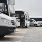 Een rij witte touringcars en busjes staat geparkeerd op een pleinachtige parkeerplaats, klaar voor een luchthaventransfer in Amerika