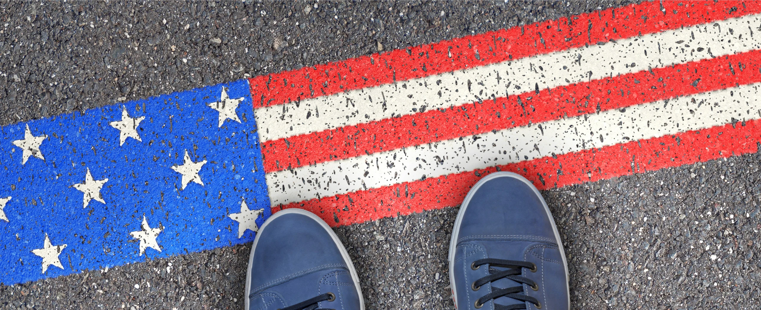 Iemand staat met blauwe sneakers op een op straat geschilderde Amerikaanse vlag als symbool voor een reis naar Amerika