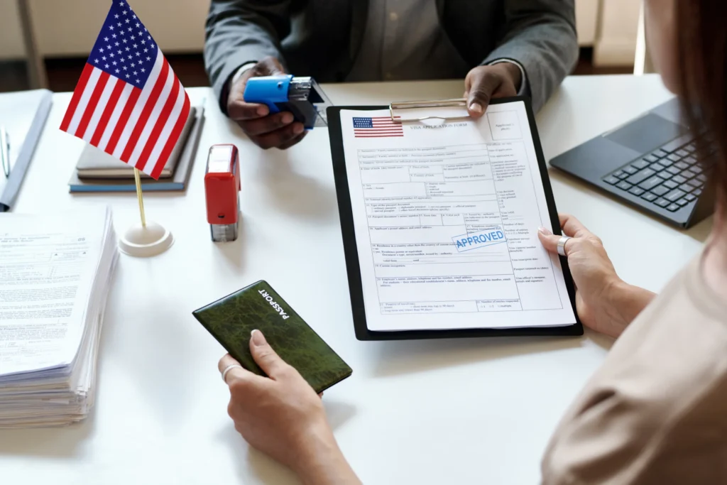 Een ambtenaar geeft een goedgekeurd visumaanvraagformulier voor de Verenigde Staten aan een vrouw die haar paspoort vasthoudt naast een Amerikaanse vlag