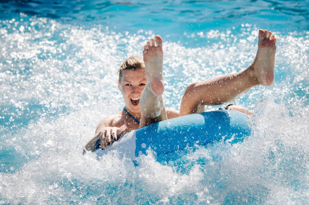 Vrouw ligt lachend op een blauwe opblaasband terwijl ze door schuimend water van een golvenbad in een waterpark glijdt