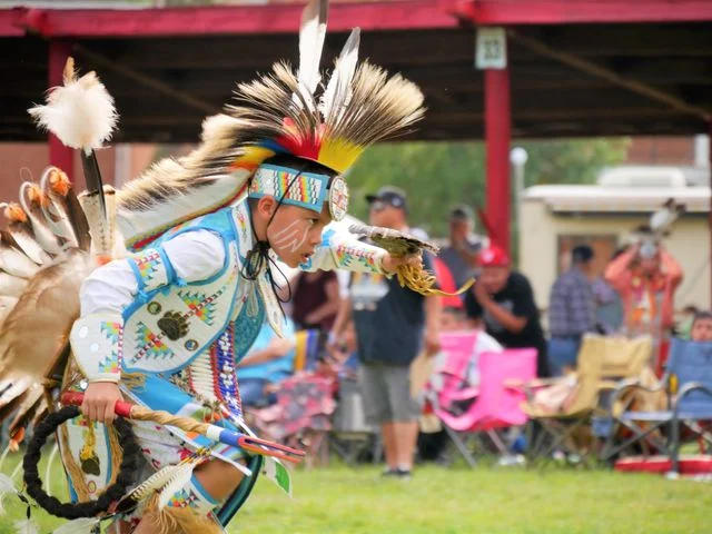 Jonge indiaanse danser in kleurrijke traditionele kleding met een verendooddak, geschminkt gezicht en kralenwerk tijdens een powwow