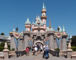 Roze en blauw sprookjeskasteel met torenspitsen in Disneyland, met bezoekers die over de brug ervoor lopen