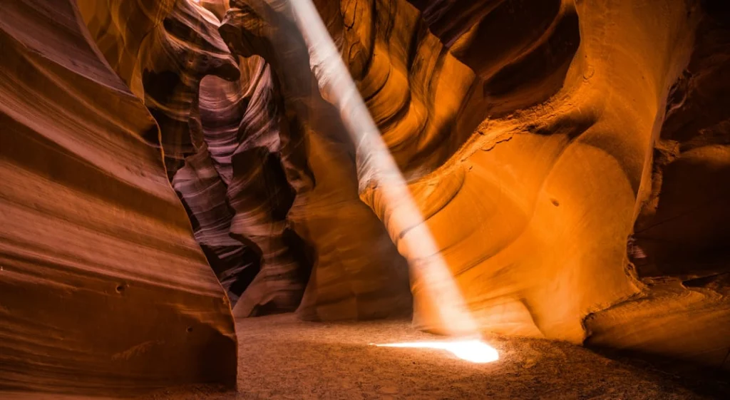 Een oplichtende golvende zandstenen vorm steekt af tegen de donkere paarsbruine wanden van de nauwe Antelope Canyon