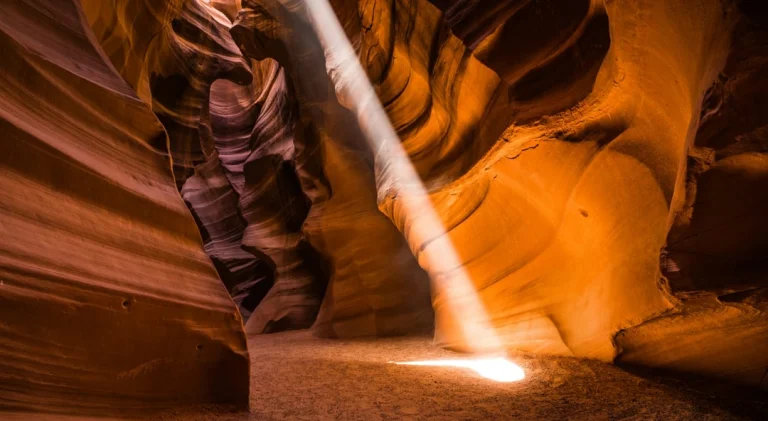 Een oplichtende golvende zandstenen vorm steekt af tegen de donkere paarsbruine wanden van de nauwe Antelope Canyon