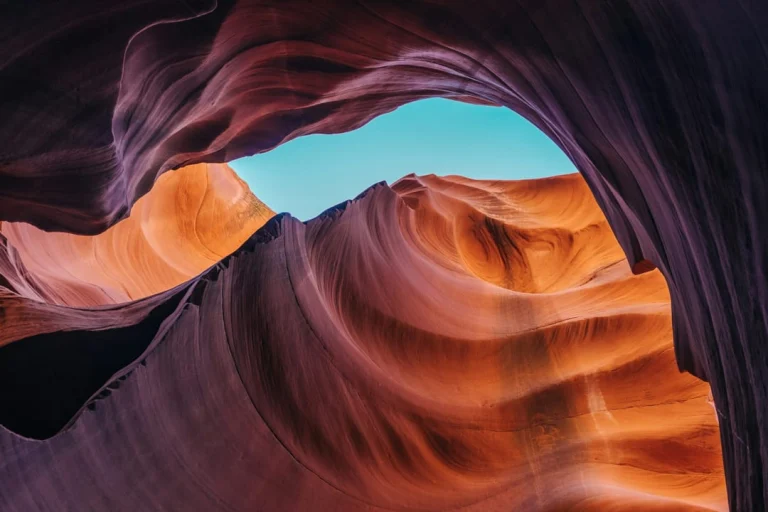 Een scherpe lichtstraal valt door een smalle opening naar beneden in de golvende oranje wanden van Antelope Canyon