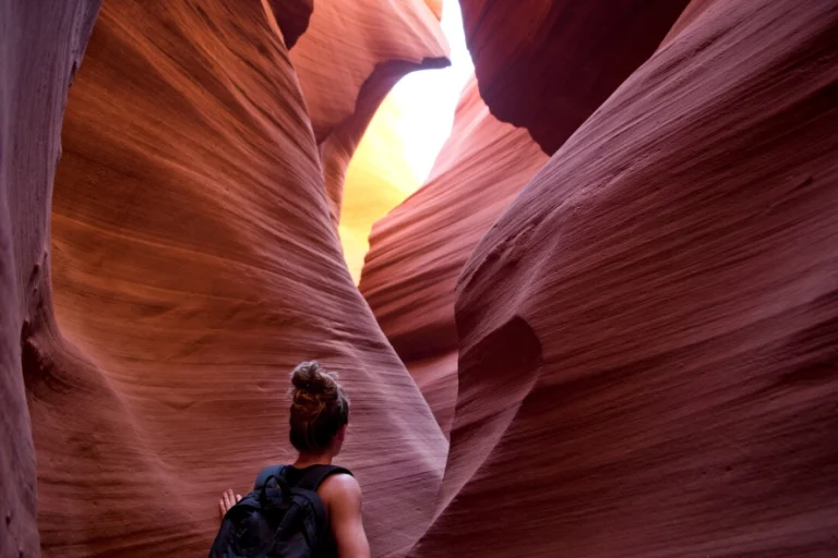 Een vrouw met rugzak loopt door de smalle, kleurrijke gangen van Antelope Canyon met licht dat van bovenaf naar binnen valt