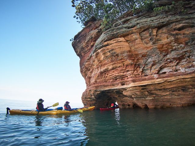 Drie kajakkers peddelen langs gelaagde roodbruine zandstenen rotswanden met zeegrotten bij de Apostle Islands in Wisconsin