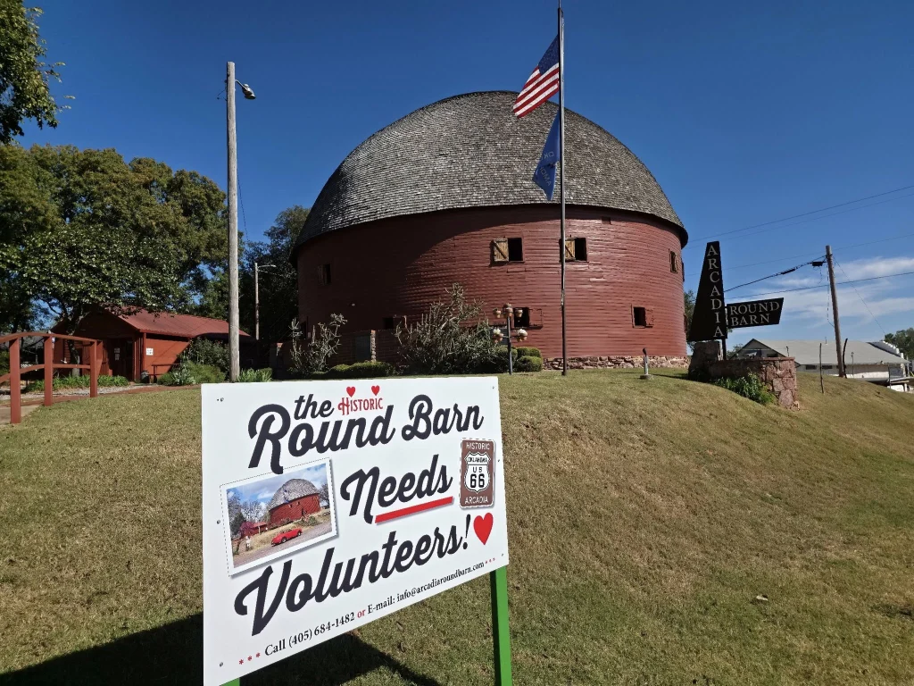Rode ronde schuur met houten dak en Amerikaanse vlag, met een bord dat om vrijwilligers vraagt op de voorgrond