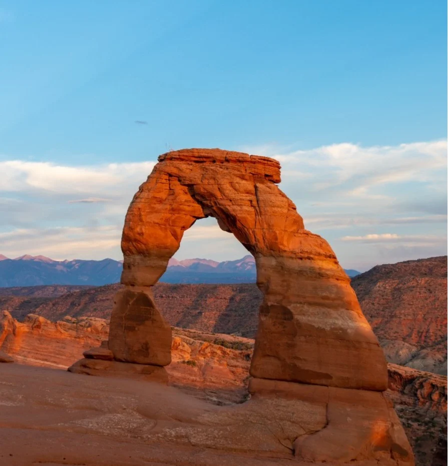 De iconische rode zandstenen boog Delicate Arch steekt af tegen bergen bij zonsondergang in Arches National Park, Utah