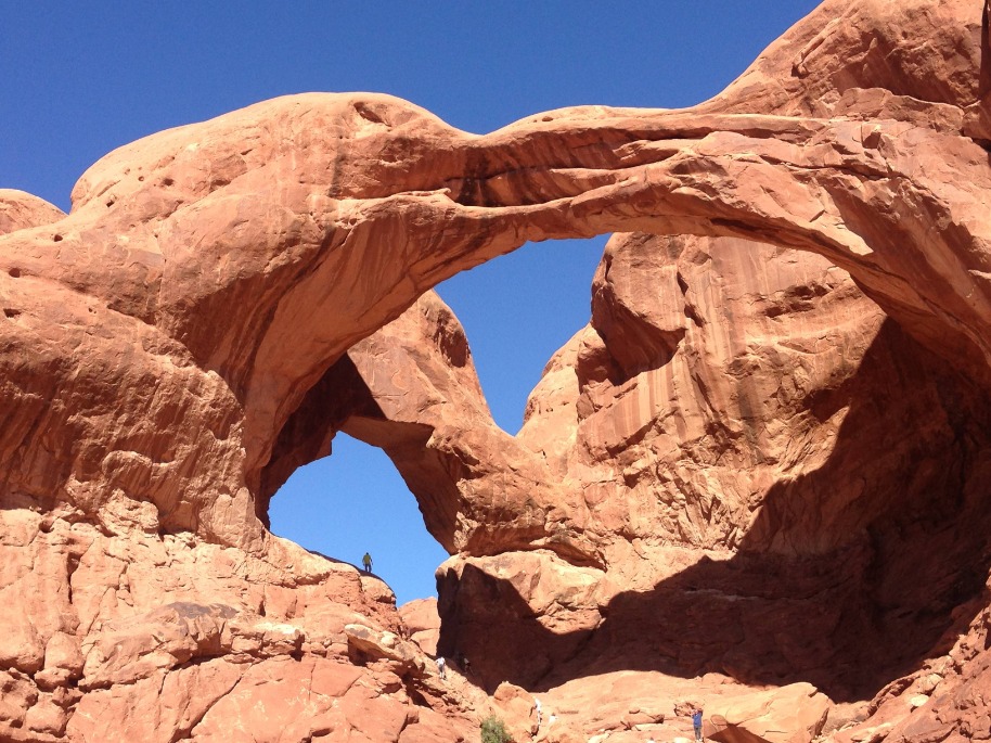 Twee samenkomende rotsbogen vormen Double Arch met kleine wandelaars zichtbaar op de rotsen eronder in Arches National Park