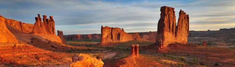Hoge rode rotsformaties en steile pilaren in Arches National Park in Utah, verlicht door het warme licht van de ondergaande zon