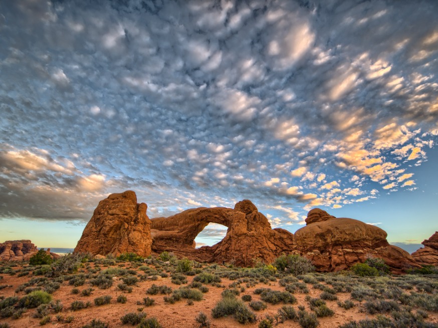 De rotsboog Turret Arch steekt af tegen een dramatische wolkenlucht met warm avondlicht in Arches National Park
