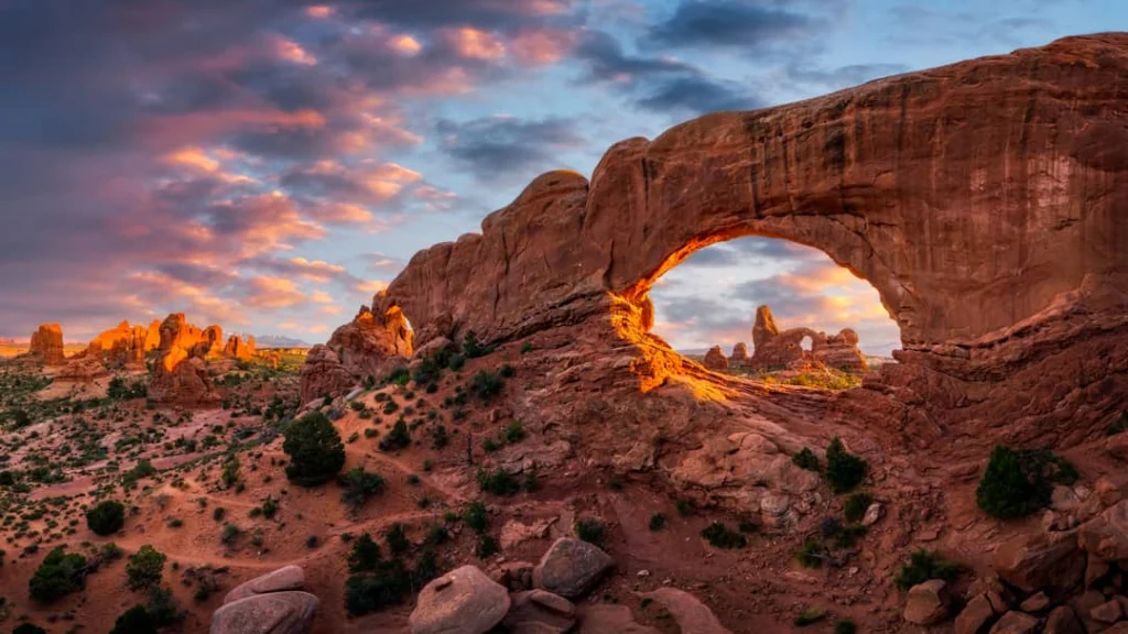 Zonlicht kleurt de zandstenen boog Turret Arch en omliggende rotsformaties feloranje bij zonsondergang in Arches National Park, Utah