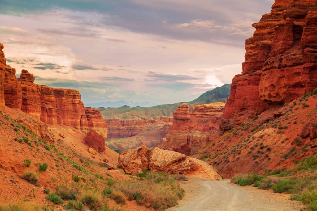 Onverharde weg tussen hoge rode zandstenen rotswanden, met bergen zichtbaar in de verte in Canyon de Chelly in Arizona