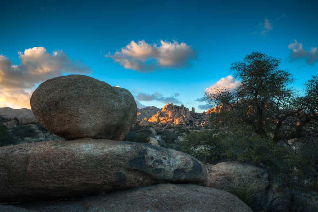Grote, gladde rotsblokken op elkaar gestapeld met bergen en struiken op de achtergrond onder een blauwe lucht in Arizona