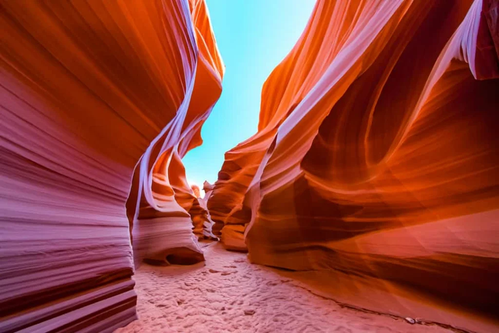 Nauwe kloof met golvende gestreepte oranje en roze rotswanden en een streep blauwe lucht bovenin, typisch voor Antelope Canyon