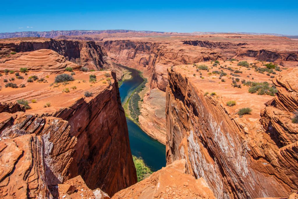 Breed uitzicht op de hoefijzervormige bocht van de Colorado rivier tussen diepe rode canyonwanden onder een blauwe lucht in Arizona