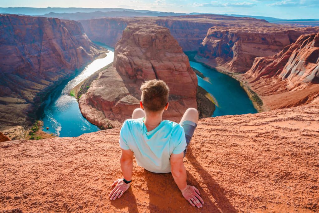 Man zit op de rand van een rotsplateau en kijkt uit over de hoefijzervormige bocht van de Colorado rivier in Arizona