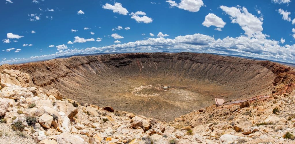 Enorme ronde krater in de woestijnbodem, gezien vanaf de rand onder een blauwe lucht met wolken in Arizona