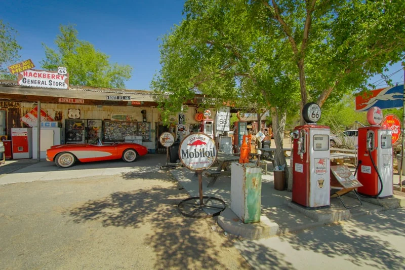 Rode klassieke cabriolet geparkeerd bij een winkel met vintage benzinepompen en reclameborden langs Route 66