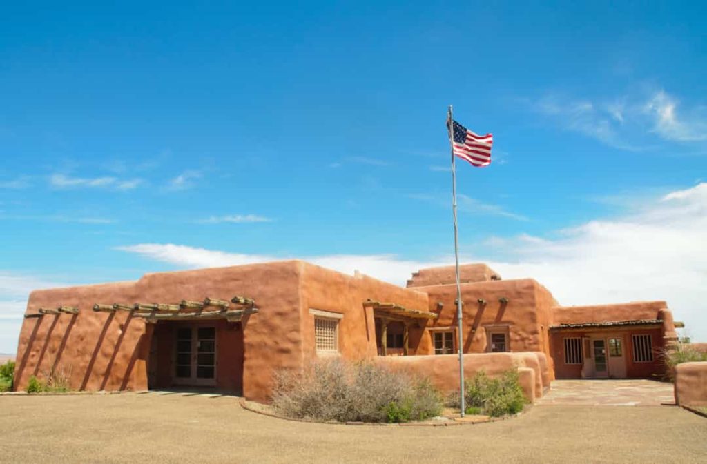 Laag adobe gebouw met houten pergola's en een wapperende Amerikaanse vlag op een vlaggenmast onder een blauwe lucht