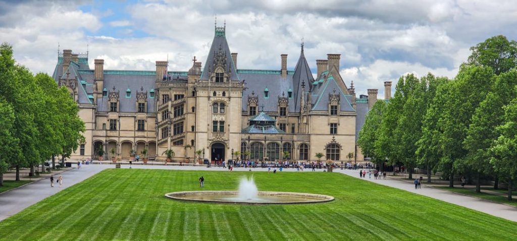 Weids uitzicht op het kasteelachtige landhuis Biltmore Estate met een fontein op het grote grasveld en bezoekers ervoor