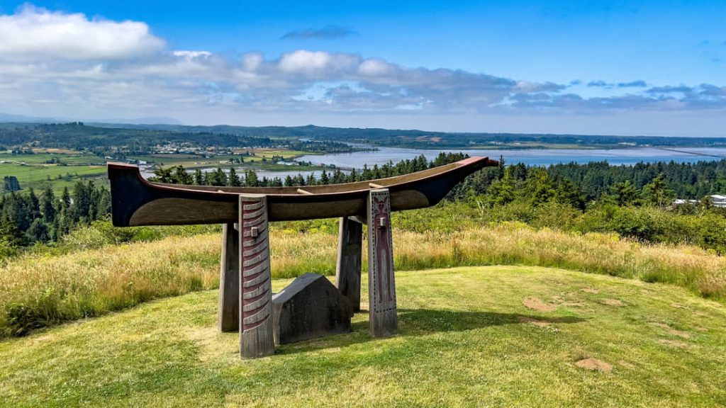 Grote houten kano opgesteld als monument op een grasheuvel met uitzicht over velden en een rivier in de verte