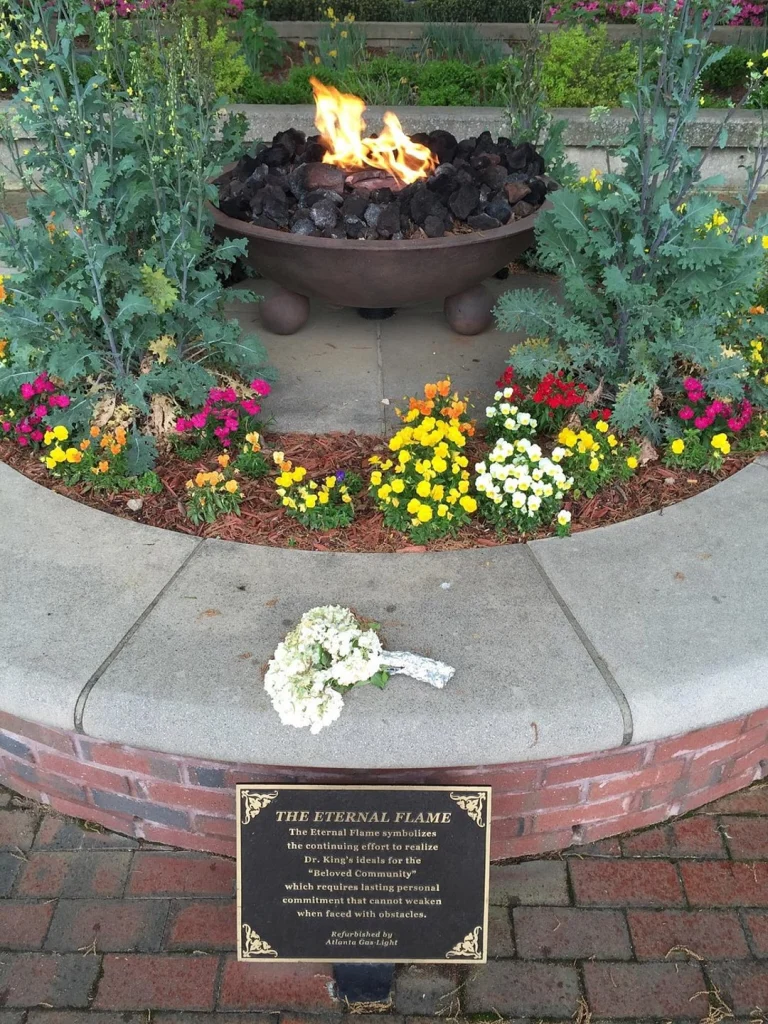 Bronzen vuurschaal met brandende vlam omringd door kleurrijke bloemen en een bosje witte bloemen ervoor als eerbetoon in Atlanta