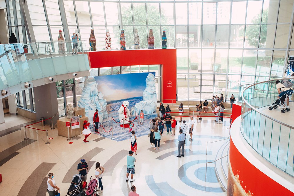 Bezoekers lopen door het lichte atrium van het World of Coca-Cola museum in Atlanta, met een rij historische colaflessen op een balkon