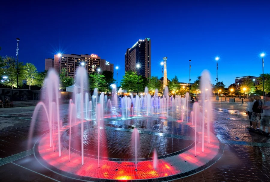 Springende fonteinstralen verlicht in rood en blauw op een plein in Centennial Olympic Park in Atlanta met de skyline op de achtergrond bij schemer