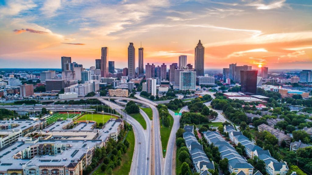 Luchtopname van de wolkenkrabbers van Atlanta met een kronkelend snelwegknooppunt op de voorgrond onder een oranje en roze avondlucht