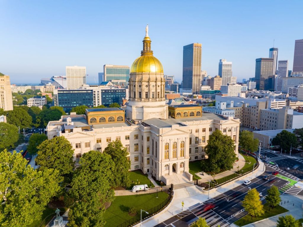 Luchtopname van het Georgia State Capitol met gouden koepel, omringd door groen en de skyline van Atlanta op de achtergrond bij zonsopgang