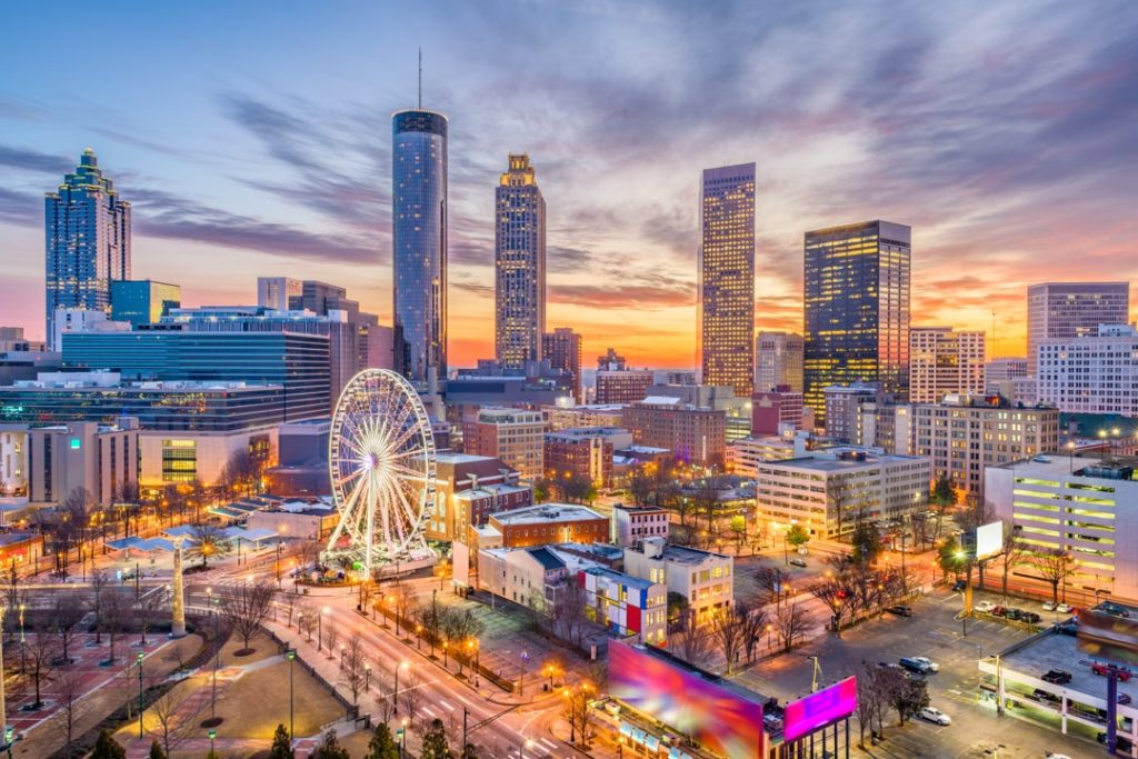 Verlichte wolkenkrabbers en een groot reuzenrad in het centrum van Atlanta tegen een roze en blauwe avondlucht