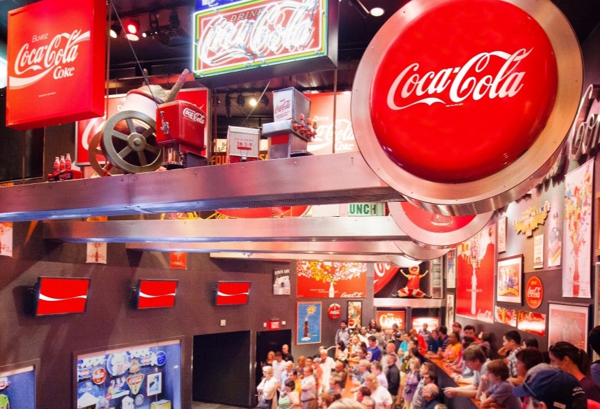 Grote ronde Coca-Cola reclame en vitrines met historische memorabilia in de museumzaal van het World of Coca-Cola in Atlanta, met bezoekers op de voorgrond