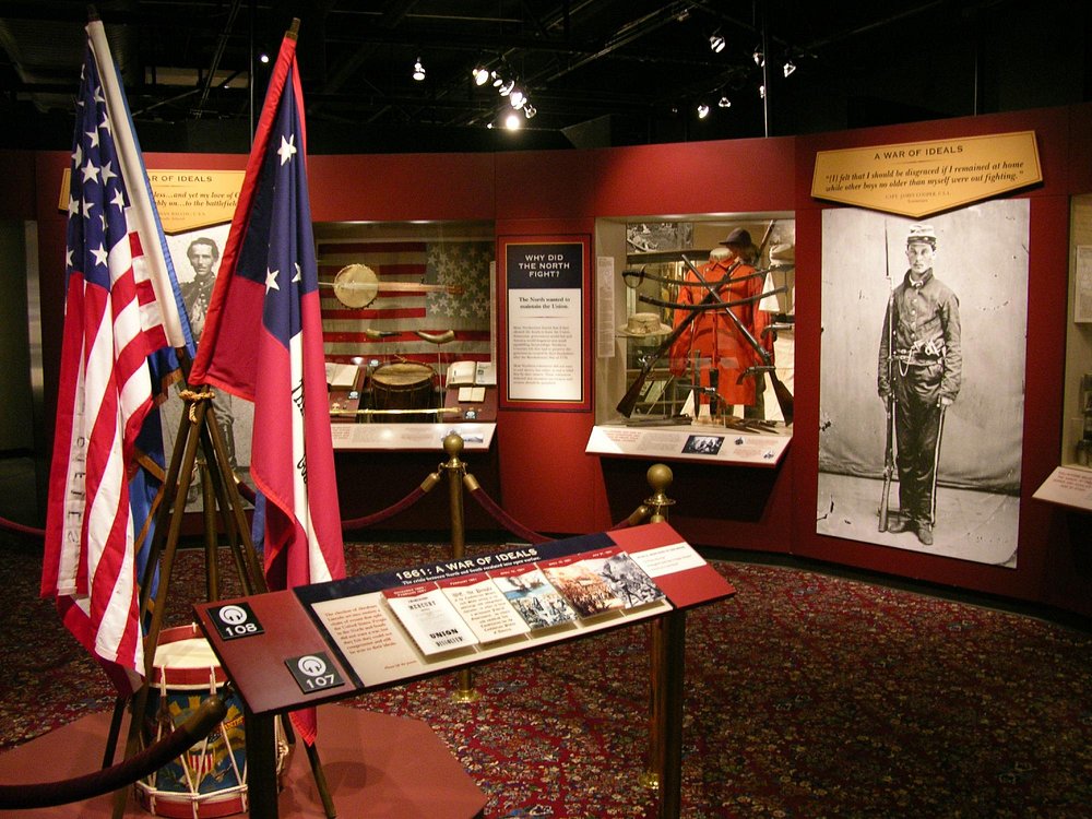 Museumvitrine met historische Amerikaanse en Confederatievlaggen, uniformen en een foto van een jonge soldaat uit de Burgeroorlog