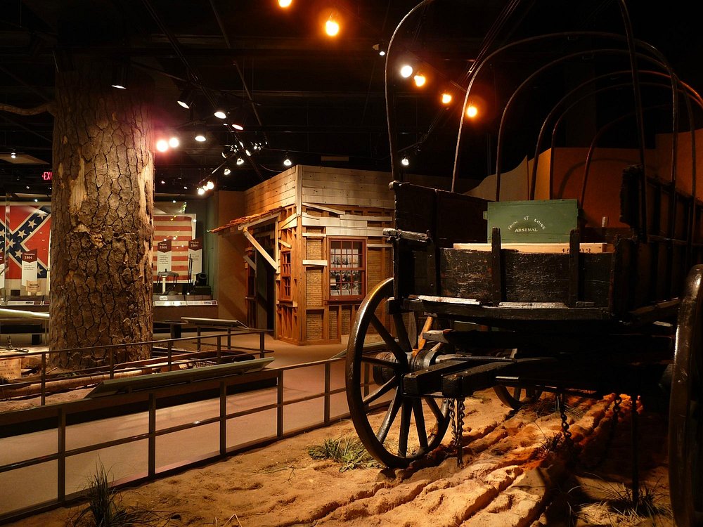 Historische huifkar en een houten gebouw in een sfeervol verlichte museumopstelling over de geschiedenis van het Amerikaanse Zuiden