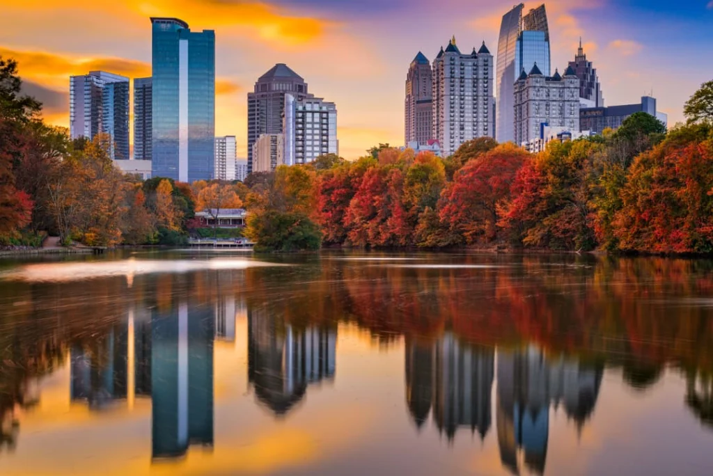 De wolkenkrabbers van Atlanta in Georgia weerspiegelen in een meer, omringd door bomen met oranje en rode herfstbladeren bij zonsondergang