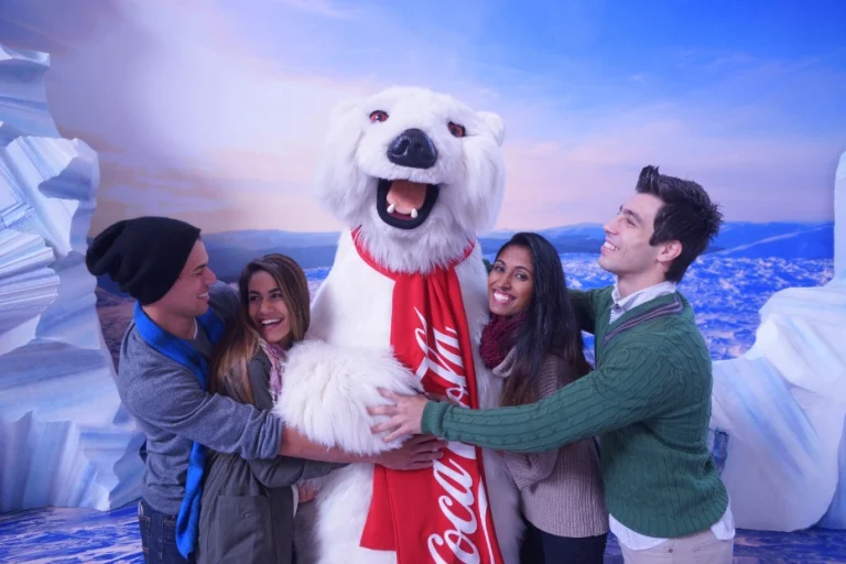 Vier lachende vrienden staan geknuffeld rond de pluizige ijsbeermascotte met rode Coca-Cola sjaal in Atlanta