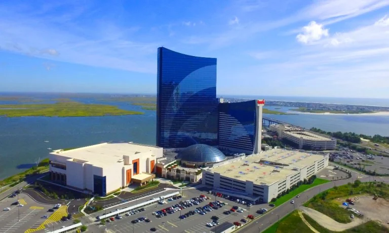 Luchtfoto van een hoge blauwe glazen toren van een casinoresort met parkeerterreinen en water eromheen in Atlantic City