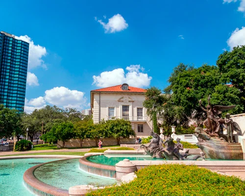 Bronzen beeldengroep in een fontein met daarachter een gebouw met oranje dak en een blauwe wolkenkrabber in Austin