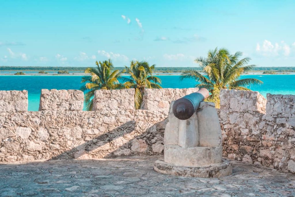 Een oud stenen kanon staat op de muur van fort San Felipe met uitzicht over de turquoise lagune van Bacalar