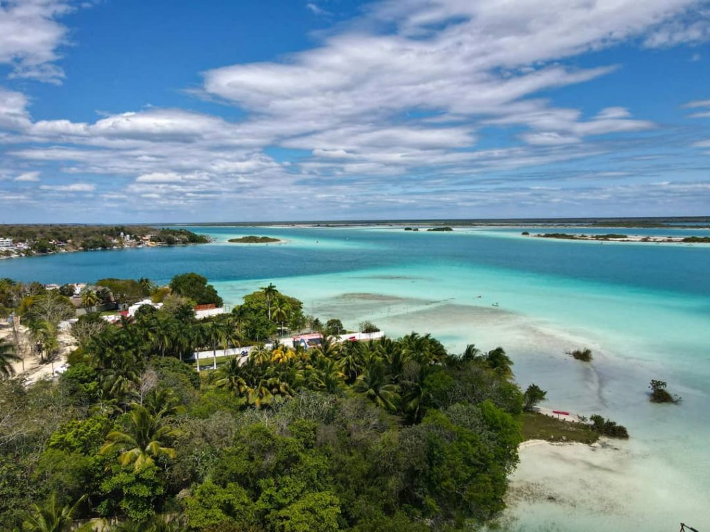 Luchtfoto van de turquoise lagune van Bacalar met zandbanken, een dorp en groene jungle langs de oever
